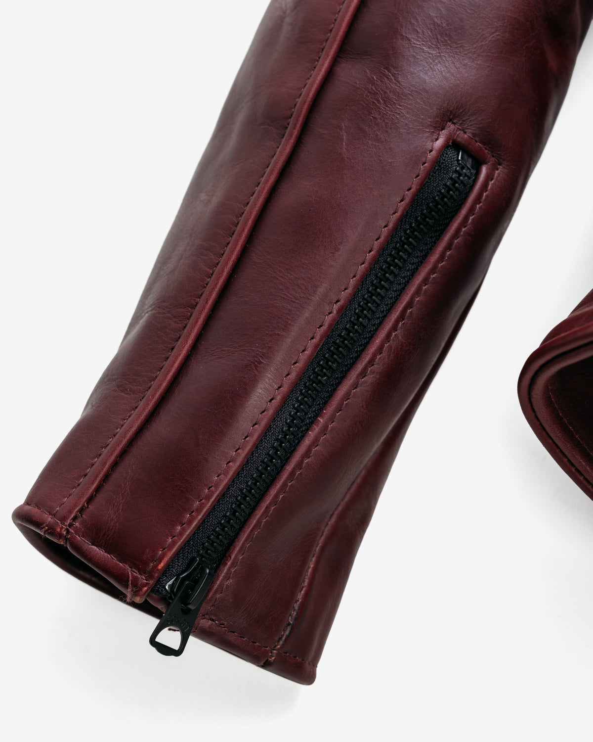 Close-up of a maroon leather glove with a black zipper on a white background