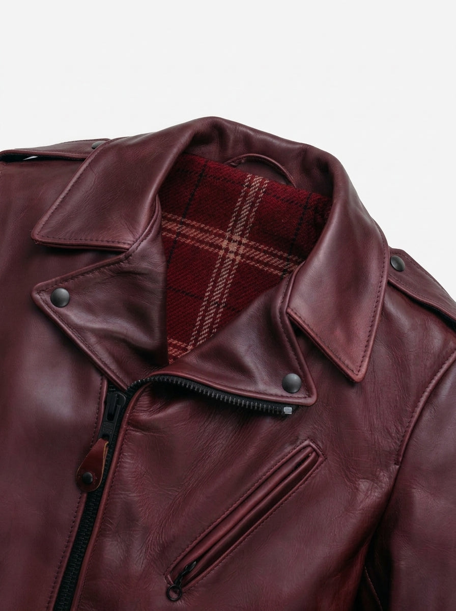 Close-up of a burgundy leather jacket with an angled snap collar, black zipper, and a red and black plaid lining visible inside the collar.