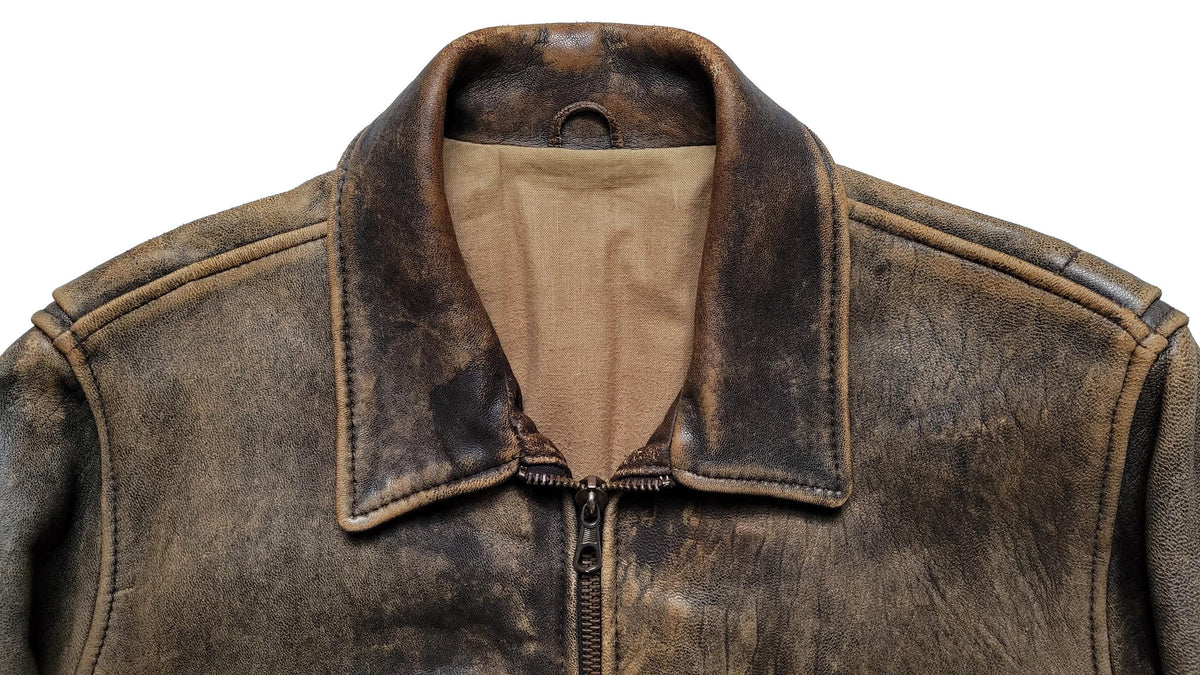 Close-up of a distressed brown leather jacket with a tan interior lining and a front zipper, shown against a plain white background.