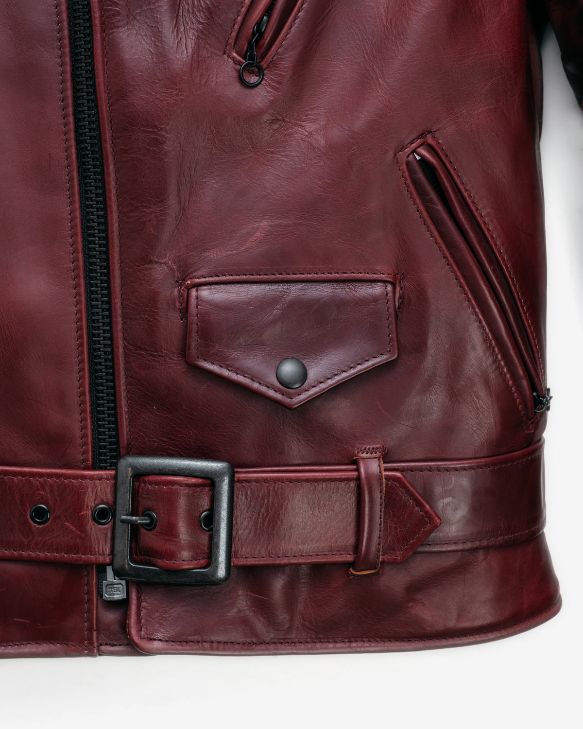 Close-up of a maroon leather jacket with a belt and zipper on a white background