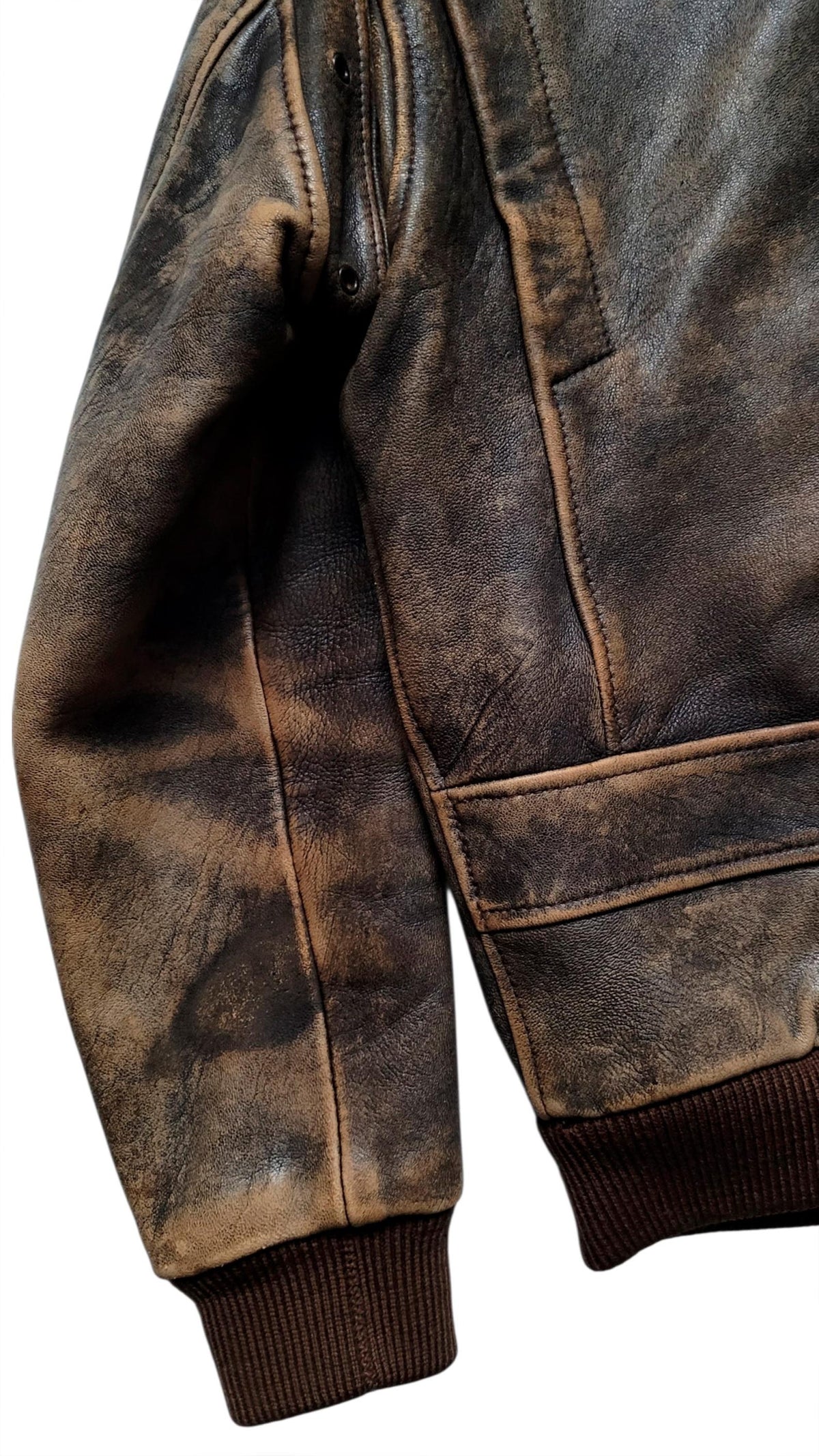 Close-up of a distressed brown leather jacket sleeve with dark ribbed knit cuffs, showing the textured leather finish and contrast stitching.