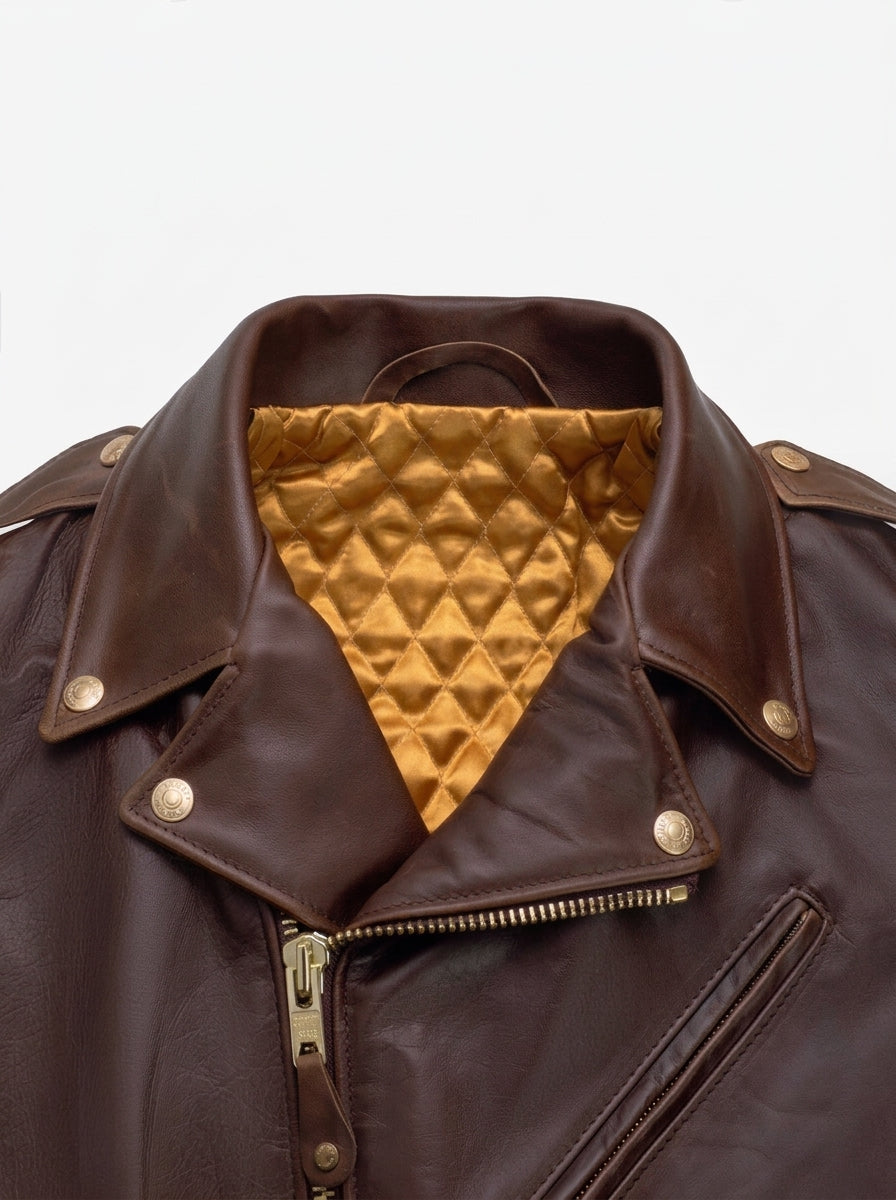 Close-up of a dark brown leather motorcycle jacket with a gold quilted interior lining visible at the open collar, featuring brass-tone snap buttons and a front zipper.