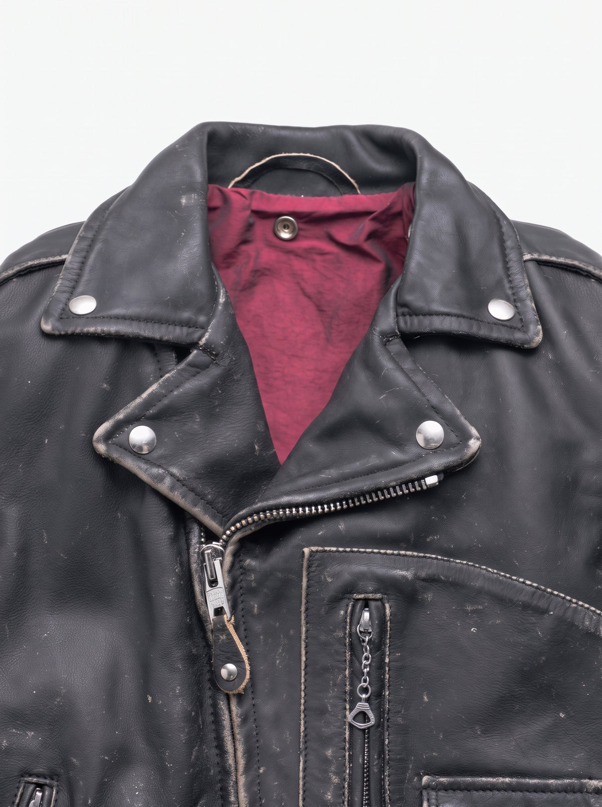 Close-up of a black leather jacket with a dark red lining visible at the collar, featuring silver metal hardware and zippered pockets.