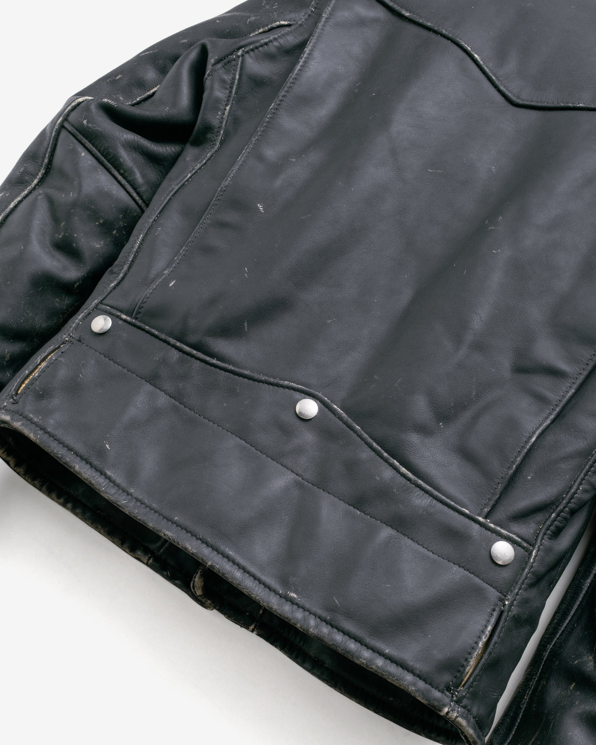 Close-up of a black leather jacket showing the chest pocket with silver snap buttons and the textured leather material.