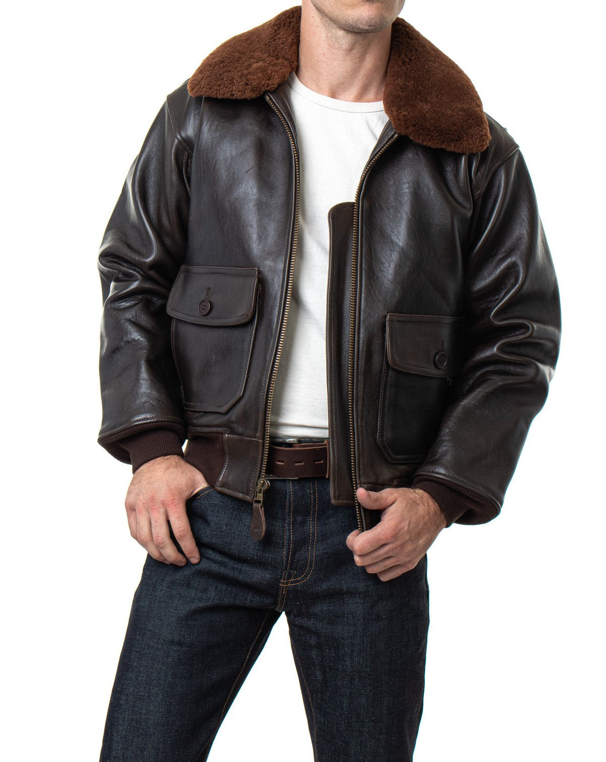 A man wearing a dark brown leather aviator-style jacket with a brown shearling collar, a white t-shirt, and dark blue jeans, shown from the waist up against a white background.