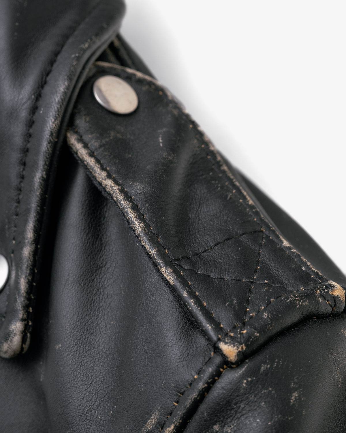 Close-up detail of a black leather jacket showing a weathered shoulder strap with silver metal rivets and visible dirt and scuffing on the leather.