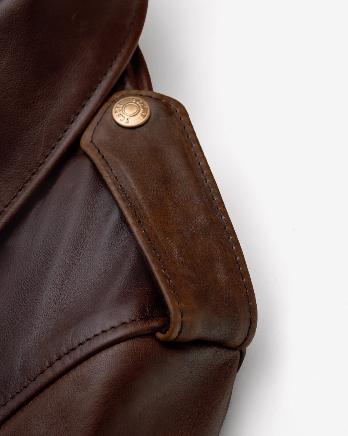 Close-up of a brown leather bag with a gold button on a white background