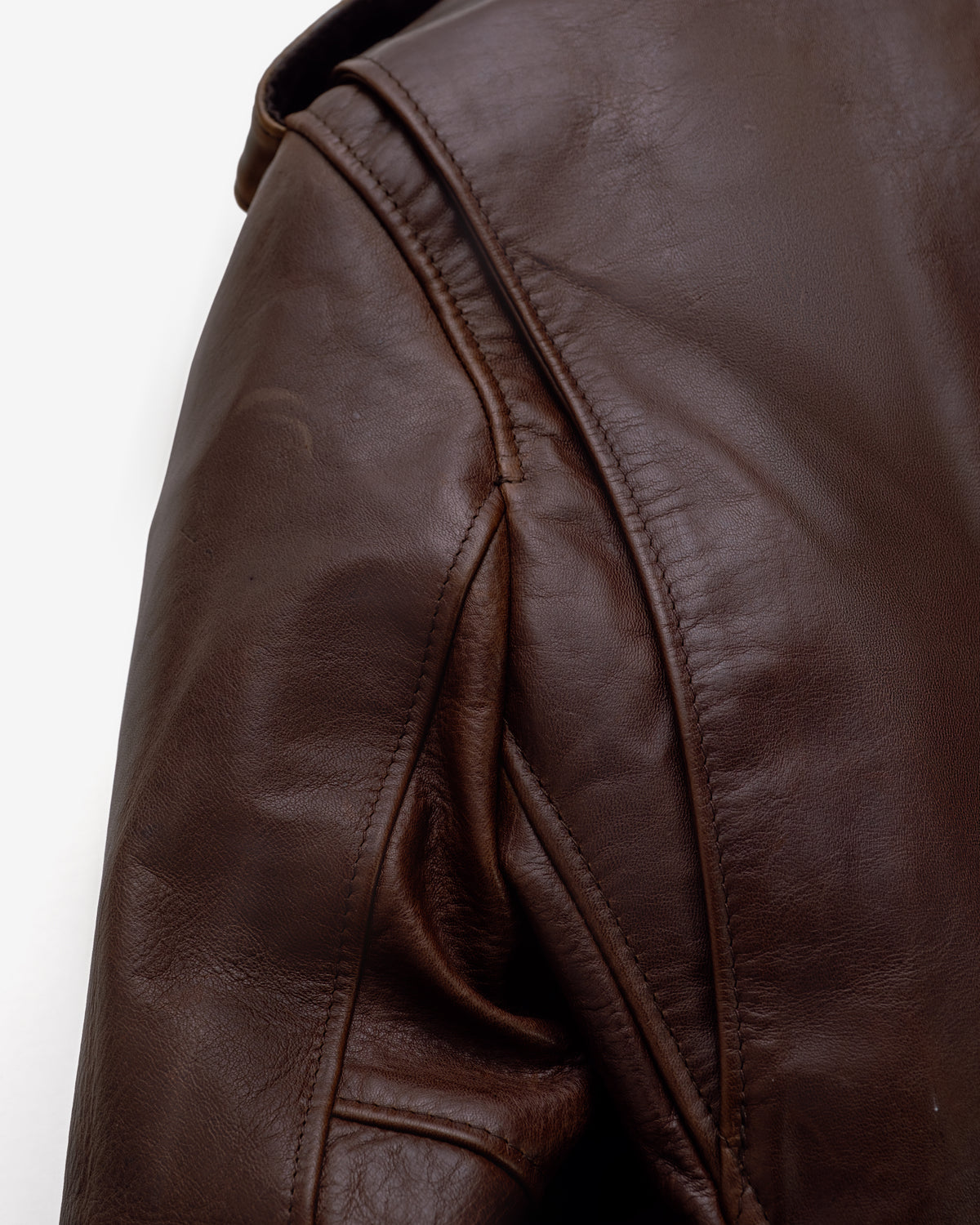 Close-up of a dark brown leather jacket showing the shoulder seam, stitching, and textured leather surface against a plain white background.