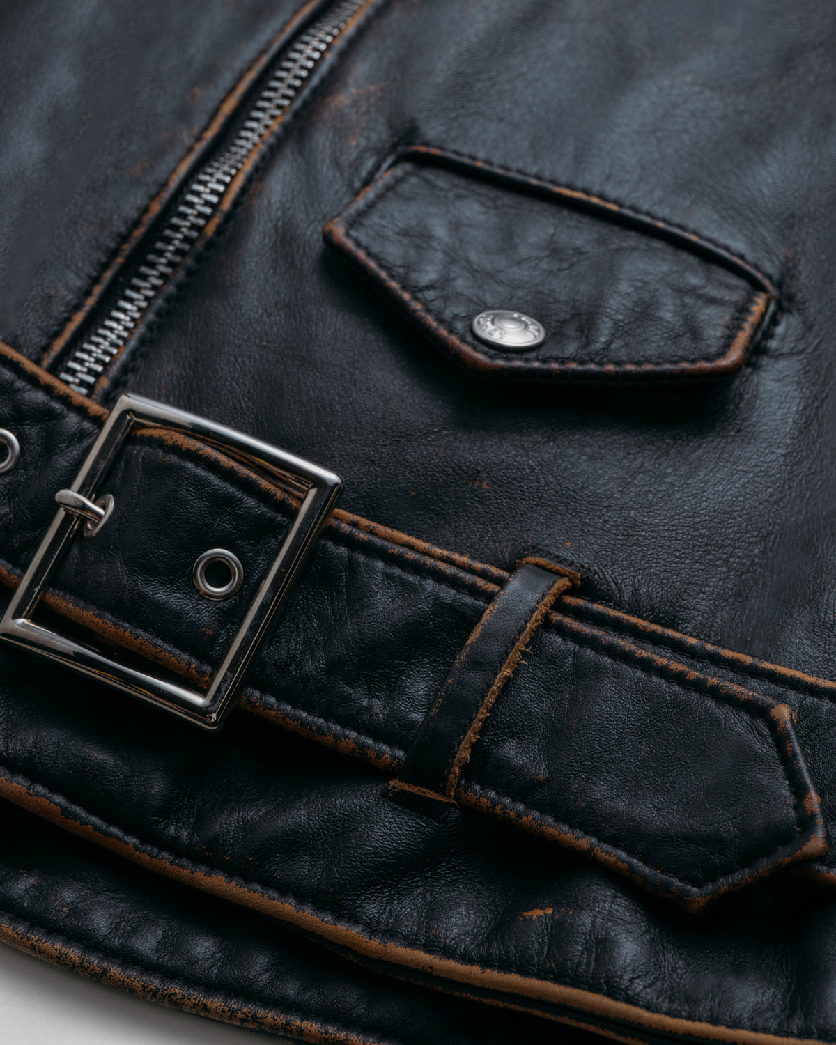 Close-up of a dark leather jacket with a zipper and buckle detail.