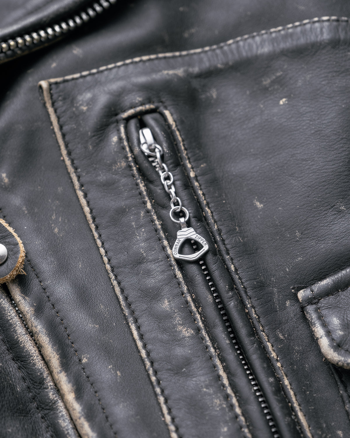 Close-up of a black leather jacket with a zipper and chain detail.